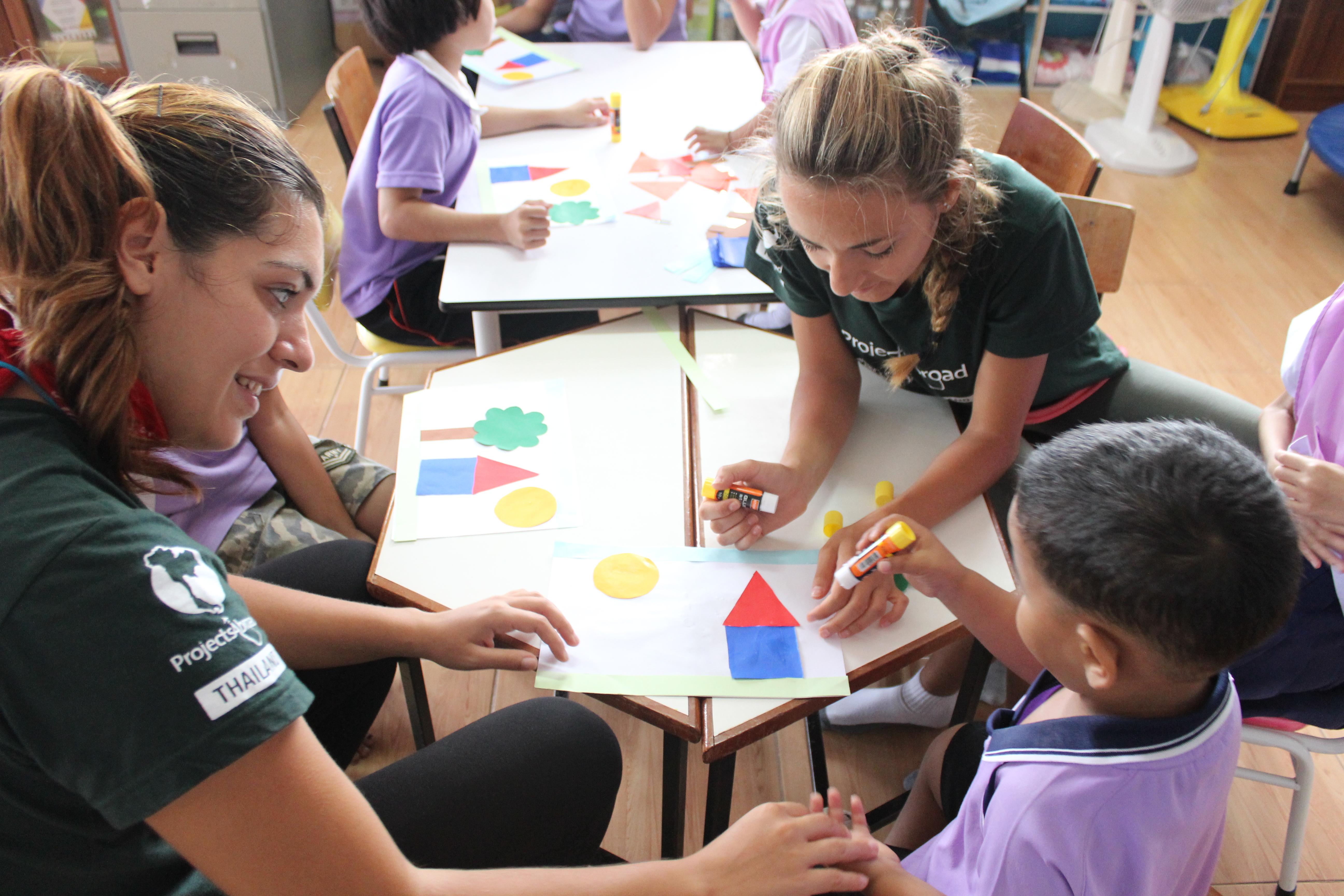 Two Projects Abroad volunteers help a small group of children with a colouring activitty at a daycare centre in Thailand. Projects Abroad Childcare volunteers work with children at a daycare centre in Thailand to complete a colouring activity.